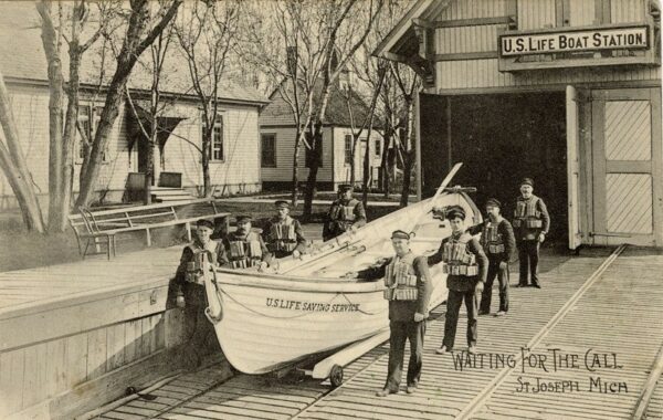 A photograph of the U.S. Life Saving Service crew posing with its surfboat in front of U.S. Life-Saving Station at St. Joseph, Michigan.