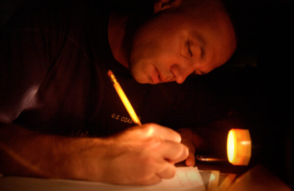 Photo: A man writing on paper by the light of a flashlight.