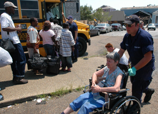 Photo: A seaman assists a woman in a wheelchair, while evacuees line up to board a school bus.