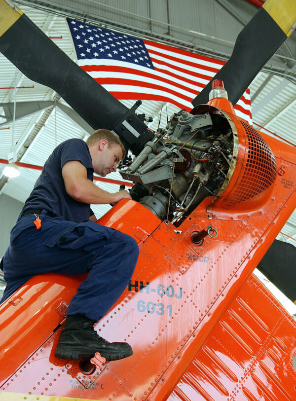 Photo: Coast Guardsman sits on the tail of a HH-60 Jayhawk helicopter while performing routine maintenance.
