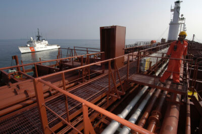 Photo: In the foreground a worker looks over the top of a motor tanker, while Coast Guard cutter sits in the background.