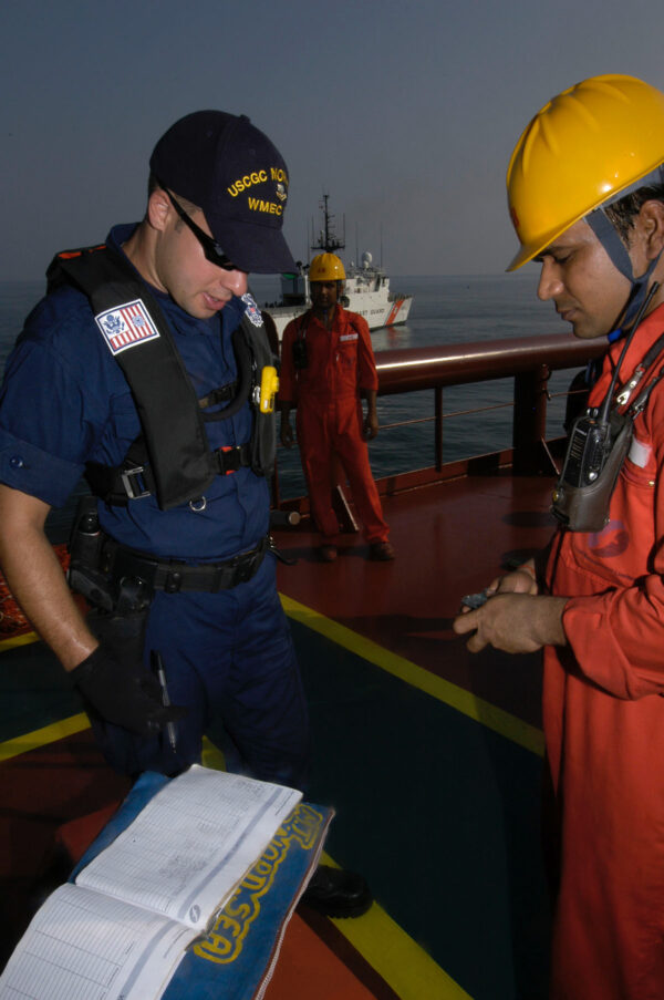Photo: A Coast Guard member signs a log book while a tanker worker looks on.