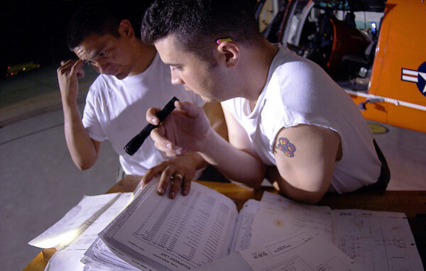 Photo: Coast Guard Petty Officers Roberto Lopez, left, and Chris Fowler refer to manuals by flashlight during the repair of a HH-65-Dolphin.
