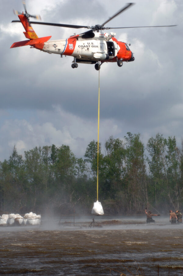 Photo: A helicopter drops a large sandbag for levee repair into a flood zone.