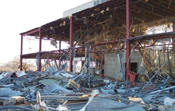 Photo: A torn up building missing its walls, surrounded by wreckage.