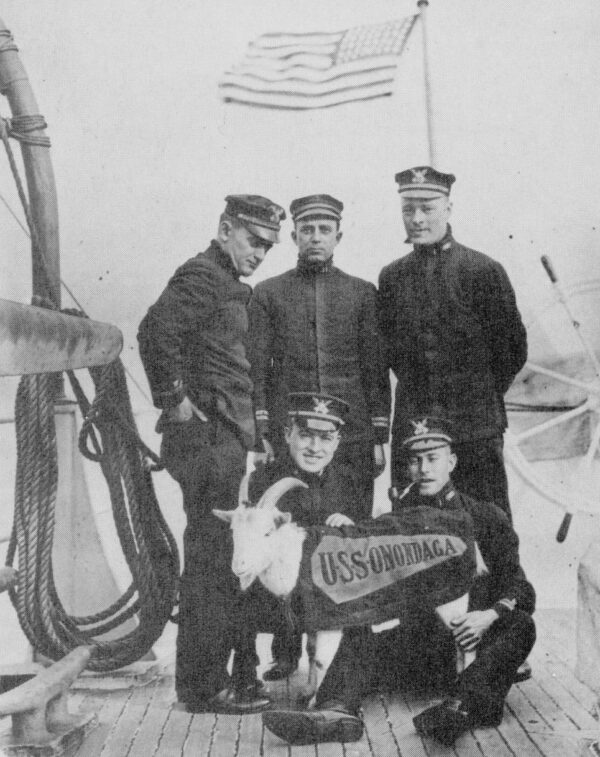 Photo: Elmer Stone (standing left) posing with other officers and goat wearing a coat with the marked “USS Onondaga”.
