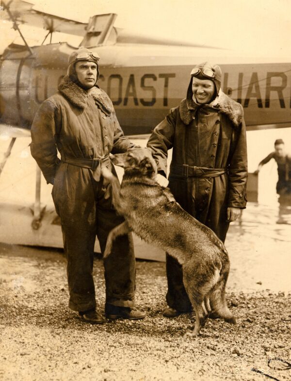 Photo: Lieutenant Commander C.C. von Paulsen, Ensign Leonard Melka, and dog Brutus pose in front of a Vought UO01 amphibious plane.