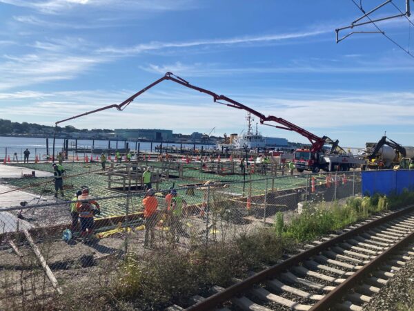 Photo: Workers stand to the side as concrete is poured over the rebar framework of the primary foundation.