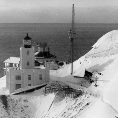 Winter-time photograph showing the old Scotch Cap Lighthouse located behind the new concrete lighthouse built in 1940.
