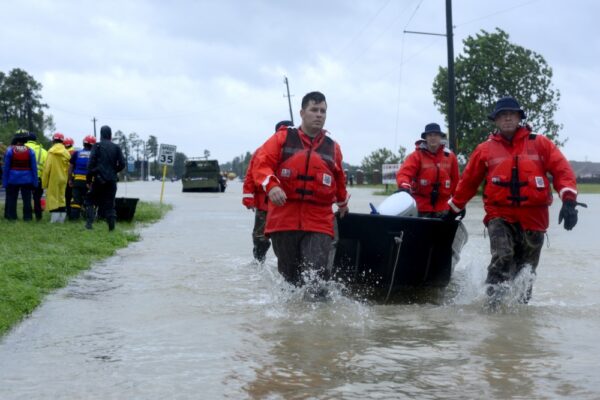 Photo: MSST members in read coats drack punt boat over flooded road.