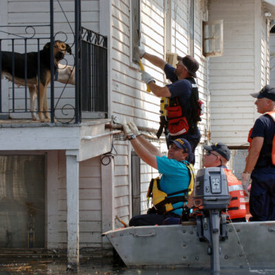 Photo: FEMA workers attempt to open a window from a U.S. Coast Guard boat, in order to rescue residents. The dogs of the house observe from the elevated porch.