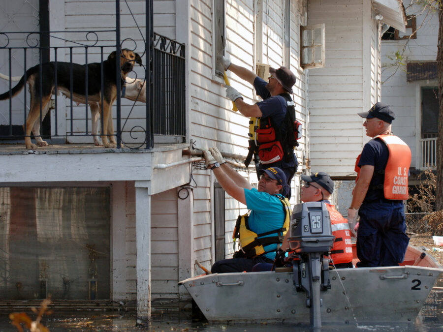Photo: FEMA workers attempt to open a window from a U.S. Coast Guard boat, in order to rescue residents. The dogs of the house observe from the elevated porch.