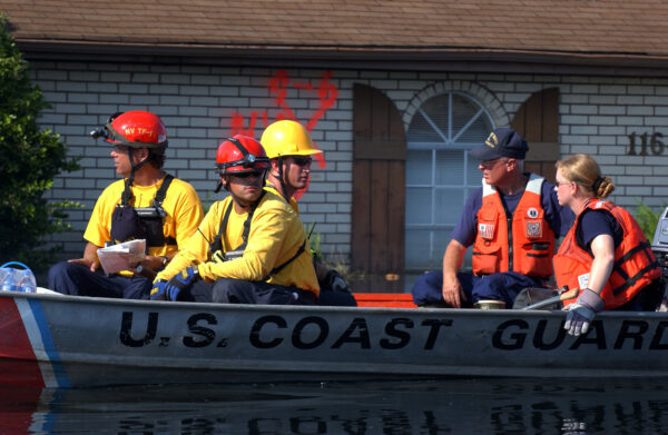 Photo: Coast Guard members pilot a boat and while local and FEMA Urban Search and Rescued workers clad in yellow search for residents in need of help.