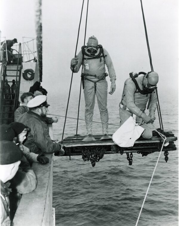 Photo: Divers in dry suits being lowered into the water.