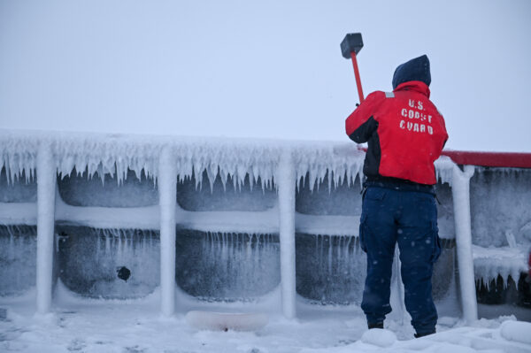 Photo: Crewman swings a large mallet to remove ice from the deck and equipment.