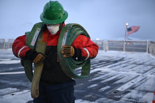Photo: Crewmember carries crane slings over his shoulders while heavy wind roars across the frozen deck.