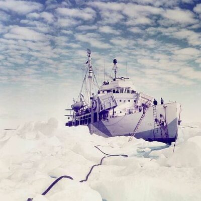 Photo: Northland sits in the ice. A ladder extends to the top of the ice, while a long rope is seen extending forward from it in a winding path through the ice.