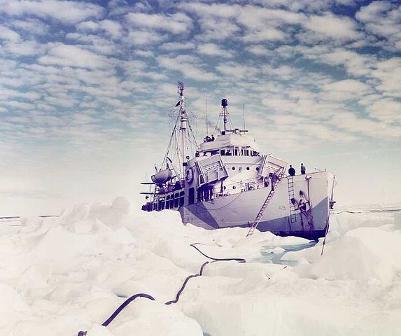 Photo: Northland sits in the ice. A ladder extends to the top of the ice, while a long rope is seen extending forward from it in a winding path through the ice.
