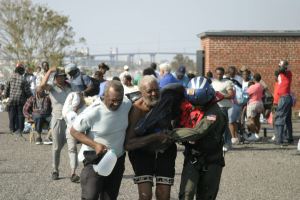 Photo: A U.S. Coast Guard aircrew member, along with another man, assists an elderly man in walking to a MH-60 Jayhawk helicopter.