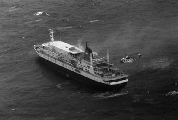 Photo: Portside aerial view of a US Coast Guard HH-3F Pelican helicopter hovers near the stern of the luxury liner Prinsendam in the Gulf of Alaska