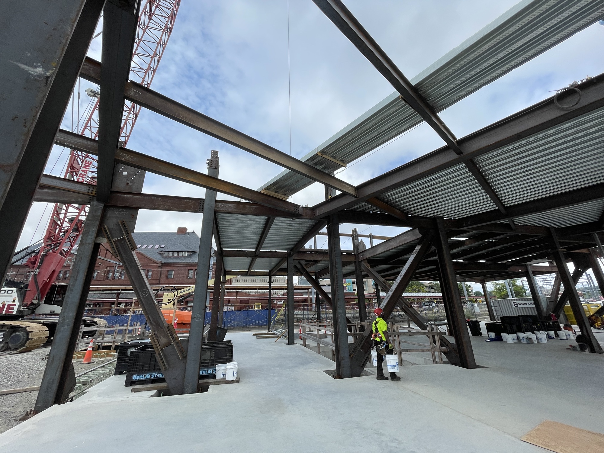 Photo: Construction worker stands next to steel framing as more material is being laid to construct the next floor.