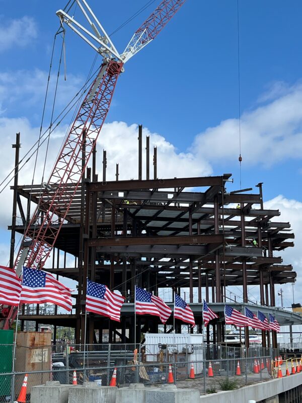 Photo: A row of American flags waving in the wind, while behind you can see already several levels of steel girders making up the frame of the new building.