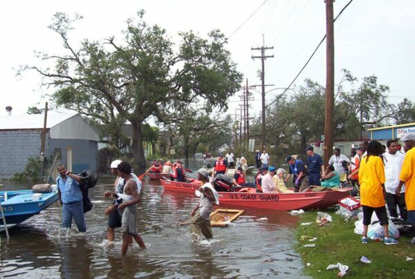 Photo: Two red Coast Guard flat boats with people in them in a flooded streets with trees in the background and people gathered all around.