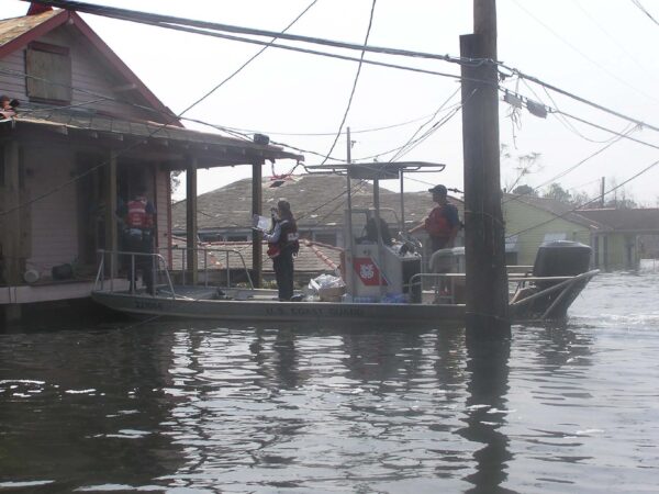 Photo: A flat boat with three Coast Guard members stops at porch of flooded home