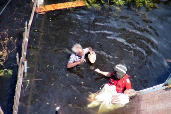Photo: A Coast Guard rescue swimmer Eric Sciubba in the water reaching towards an elderly man.