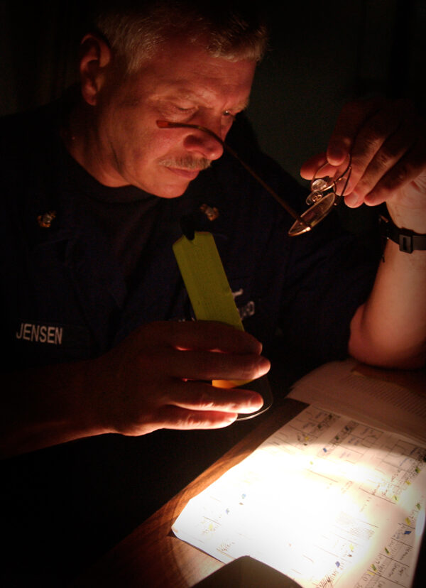 Photo: CPO Garth Jensen reads paperwork by flashlight.