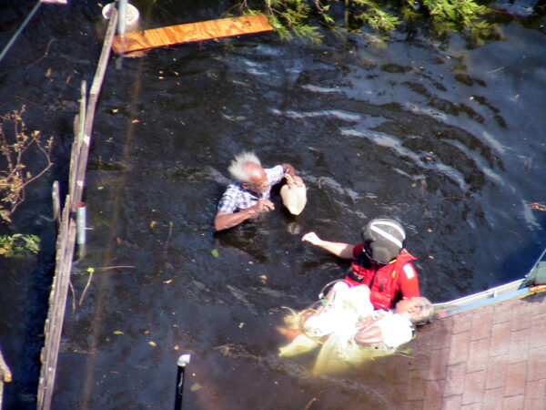 Photo: Aerial view of a rescue swimmer preparing an elderly man and woman for transport to safety.